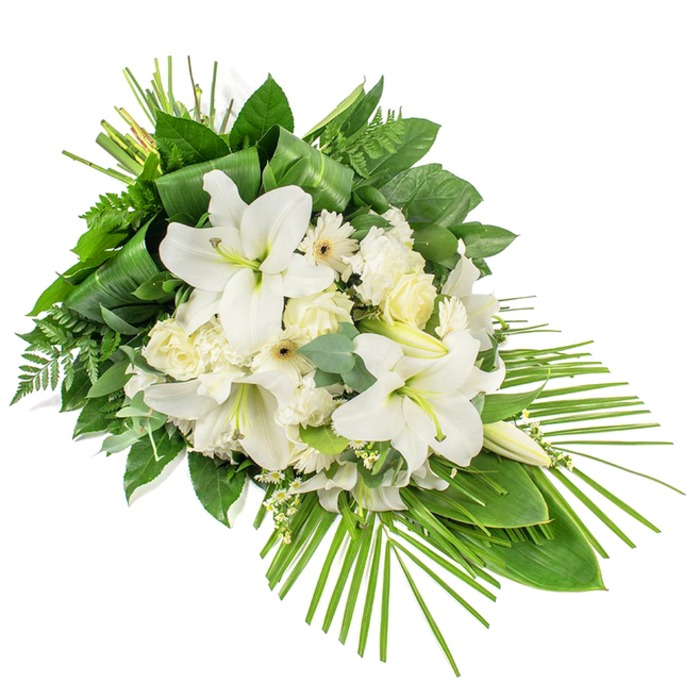 A long, tear-shaped funeral arrangement is presented diagonally on a plain white background, the design gradually tapering from a fuller top left to a slender, pointed base at the lower right. The eye is immediately drawn to the cluster of large, white Oriental lilies at the heart of the spray, their open petals smooth and slightly curved, opening outward to expose delicate, pale-green stamens. Alongside them, creamy white roses and softly ruffled carnations nestle together, forming a lush, cushioned centre. Interspersed with these larger blooms are white gerbera-style flowers with finely cut petals and modest cream or pale-yellow centres, providing a fresh, daisy-like contrast. Threads of small white filler flowers run through the design, lightening and blending the individual elements into a harmonious whole. Surrounding this floral centre is a frame of assorted greenery: broad, dark green leaves reflect a gentle shine; fern fronds offer feathery texture and a slightly informal, garden-like feel; while disc-shaped eucalyptus leaves in muted blue-green contribute a subtle colour shift and rounded form. Long blades of foliage are wrapped and bound into tidy bundles near the top of the piece, guiding the eye upward, and a sweeping fan of slender palm fronds extends from the lower right, accentuating the arrangement's flowing, elongated silhouette. The overall impression is of calm, purity, and quiet dignity, much like the stillness around Stanmore's churches and community spaces before a service begins. Designed as a one-sided display, this spray would be appropriate for a funeral, cremation service, or memorial gathering, providing a serene floral tribute to be delivered throughout Stanmore and nearby neighbourhoods.