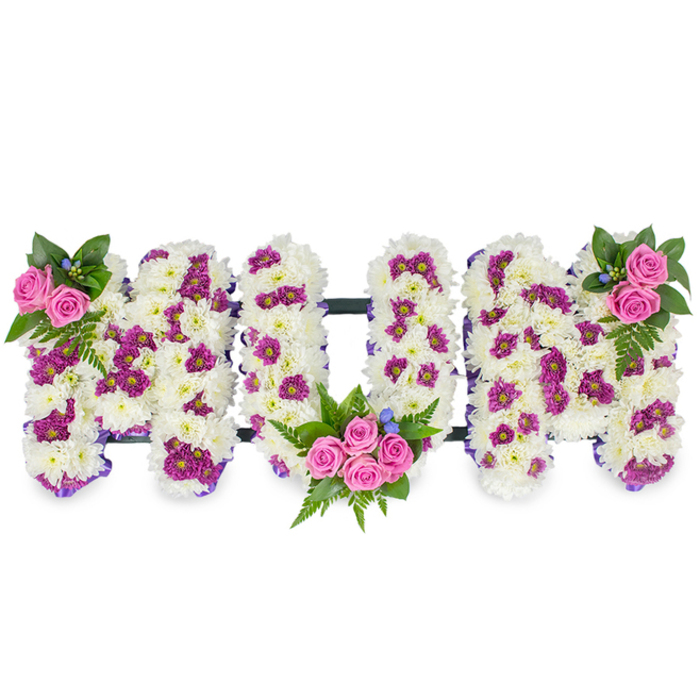A heartfelt memorial arrangement spelling MUM in three large, raised letters, photographed against a neutral white background so the composition reads with clarity and compassion. Each letter is densely covered in pristine white chrysanthemums, creating a soft, pillowy texture that conveys purity and calm. Speckled through the white are clusters of vivid purple and magenta spray chrysanthemums which give gentle contrast and visual movement across the letters. Small, vibrant pink spray roses punctuate the design as focal islands of colour: the first M wears a small, elegant cluster at its upper left, complete with rich green foliage and ferns and a few tiny blue accent blooms tucked in for a cool highlight. The U cradles a more prominent bouquet within its lower curve, where four to five pink roses bloom amid abundant dark green leaves and slender fern fronds, creating a sense of shelter and warmth. The second M echoes the first with a matching rose cluster at its upper right. Subtle, dark horizontal bars connect the three letters along their bases, suggesting framework and cohesion without being obtrusive. Under soft, diffused lighting the chrysanthemums appear almost cloud-like, the pink roses offer a tender perfume and visual softness, and the magenta accents draw the eye gently around the form. This traditional yet carefully personalised tribute is appropriate for funeral services, wakes, or memorial gatherings in Stanmore - often chosen for deliveries to venues around Bentley Priory, Canons Park, or local family-run chapels - conveying love, honour, and remembrance with understated craftsmanship.