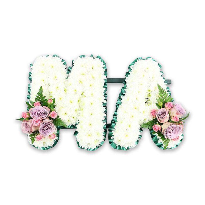 A beautifully composed letter tribute spells MA in flowers, a fitting farewell for a beloved mother, nanny, or Mama whose presence is treasured by family and friends. Each capital letter is filled edge to edge with compact white chrysanthemums, their rounded petals overlapping so closely that they form a luxuriously soft, cushiony surface. The whiteness of the flowers is clean and luminous, evoking a feeling of peace and gentle remembrance, as if the arrangement has been designed to cradle precious memories. The outline of both the M and the A is traced by a deep emerald green satin ribbon, folded into neat pleats and ruffles that create a textured border. This green trim gives the letters definition and shape, ensuring they stand out clearly even from a distance, whether placed inside a chapel or outside at a burial service around Stanmore's leafy streets. A slim horizontal bar in the same dark green hue subtly connects the two letters, so they sit together as one complete design. At the lower base of the left side of the M and the right side of the A, matching floral clusters introduce soft colour: lilac and pink roses in varying stages of openness, accompanied by smaller pink spray roses that add fine detail and depth. A single fern frond arcs gently through each cluster, its feathered texture bringing a touch of natural woodland grace. Photographed against a plain white background, this MA tribute appears calm, balanced, and carefully considered, the sort of arrangement a local Stanmore family might choose for a funeral at a nearby church, synagogue, or crematorium as a touching, personalised expression of love and respect.