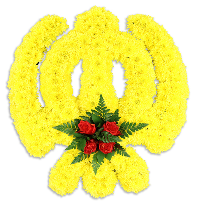 Dominating the frame is a carefully constructed Khanda, its familiar circular and sword motifs shaped from a dense sea of bright yellow chrysanthemums that have been placed bloom by bloom to preserve the emblem's crisp silhouette. The chrysanthemums' ruffled petals create soft ridges and gentle shadows across the surface, lending the piece a tactile, three-dimensional quality that reads as both bold and tender. Where the emblem's arms converge, five deep red roses form a compact, jewel-like centre; their smooth, velveteen petals are cushioned by dark green fern fronds, which provide textural contrast and a cooling visual border to the warm yellow. The artwork rests against a plain white background and casts a subtle grey shadow, signaling that this is a substantial, physical floral tribute-likely mounted on a base for display at a memorial table or ceremony. Light skims the topmost petals, brightening the yellows and deepening the rose tones, while the imagined scent is a soft, green floral hush rather than something heady. The arrangement feels rooted in local tradition and respect, the kind of piece an experienced Stanmore florist would create for commemorations near Stanmore Common or services across Harrow, where colour and form speak quietly of honour, remembrance and community care.