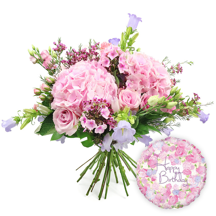 This carefully composed image presents a lush birthday bouquet paired with a festive balloon, both placed against a clear white background so each detail of the arrangement is easy to imagine. The bouquet is full and domed, built around several prominent heads of blush pink hydrangea. Each hydrangea flower appears as a soft sphere of densely packed, velvety petals, creating an impression of romantic abundance. Interspersed among these are soft pink roses at different stages of opening: some display wide, layered rosettes of petals, while others remain as smooth, tightly furled buds, adding a dynamic, living quality that would unfold day by day in a Stanmore living room. Threaded between the larger blooms, diminutive clusters of bright fuchsia-pink filler flowers-resembling waxflower-add sparkle and texture, their tiny blossoms deepening the pink colour story. Slender stalks of campanula rise gently above the rounded bouquet, each bearing small, bell-shaped flowers in lavender and periwinkle shades, adding a cool, vertical accent reminiscent of dusky skies above Stanmore's suburban rooftops. Surrounding everything is a collar of fresh green foliage, ranging from narrow, upright leaves to broader, darker greens, bringing a sense of natural structure and garden freshness that echoes local hedgerows and park borders. The stems are gathered neatly at the base, left visible to show the bouquet's hand-tied construction, as if just finished on a florist's bench near Stanmore Broadway. To the lower right, a round foil Happy Birthday balloon with a light metallic sheen acts as a joyful companion piece. Its surface is adorned with an intricate pattern of tiny roses and buds in soft pinks, creams, and light purples, framing the words Happy Birthday written in a flowing purple script font. Together, the arrangement and balloon evoke a complete birthday gesture, perfect for a celebration at home, a family meal at a local restaurant, or as a thoughtful delivery anywhere across Stanmore.