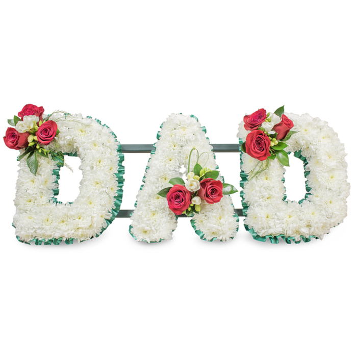 Presented against a bright white backdrop, this bespoke sympathy display spells the word DAD in three large, sculpted letters, each surface densely layered with immaculate white chrysanthemums to create a uniform, soft texture that conveys serenity and purity. A deep emerald-green pleated ribbon crisply outlines every letter, accentuating the negative space between strokes and lending a measured formality to the composition. Each letter is thoughtfully embellished with a compact, richly coloured spray of deep red roses and delicate white freesia; the roses-shown in varying stages from bud to part-open-bring a sense of warmth and lasting affection while the freesia adds a whisper of brightness and a delicate perfume. Verdant foliage tucks around each spray, and on the central A a tasteful loop of fresh green foliage reaches upward, introducing a graceful vertical line amid the horizontal flow. Behind the blooms, slender dark green or black metal bars are visible at the base, discreetly providing structural support and ensuring the letters sit evenly when displayed at a funeral venue. The colour story-pure white chrysanthemum set against jewel-like red roses and emerald accents-reads as both traditional and deeply personal, making this a classic choice to honour a father or patriarch. As an experienced local florist serving Stanmore and surrounding Harrow neighbourhoods, Flower Delivery Stanmore often recommends this style for family-led memorials along Stanmore Broadway or intimate ceremonies near the local parish, where the arrangement's calm dignity and tactile detail can be properly appreciated.