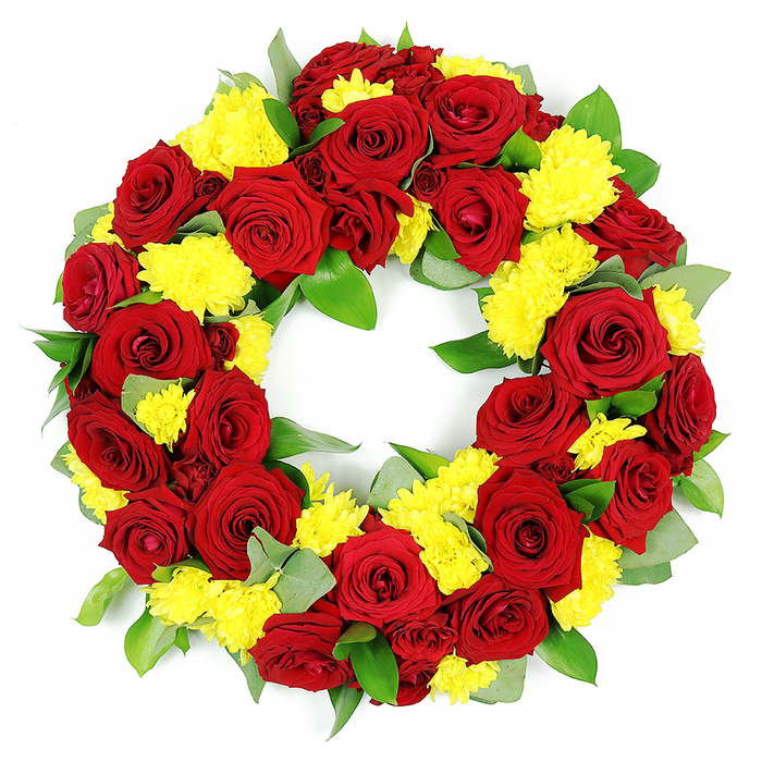 A beautifully detailed circular funeral wreath fills the frame, photographed against a pure white background so that its rich colours and textures are clearly defined. The wreath is tightly constructed, creating a continuous ring of flowers with an open centre that symbolises unending remembrance. Deep red roses form the main body of the design. Each rose is captured in full bloom, with smooth, velvety petals unfolding from compact centres into layered spirals, revealing slight tonal shifts from ruby red to darker burgundy along the outer edges. Woven between these roses, bright yellow chrysanthemums-likely spray or button forms-add a vivid contrast. Their myriad thin petals create rounded, fluffy heads that sit a little higher than the rose blooms, making the surface of the wreath gently undulate. The yellow flowers bring a gentle warmth and hint of hope, softening the intensity of the deep reds. All of this is supported by a bed of foliage: glossy, dark-green leaves nestle around and behind the blossoms, while paler, silvery-green sprigs suggest eucalyptus, lending a natural, airy touch and preventing the design from feeling heavy. The lighting is soft yet bright, eliminating shadows and drawing attention to each curve of petal and subtle vein in the leaves, as though the wreath has just been placed on a tabletop in a Stanmore workshop near The Broadway or close to the green spaces around Bentley Priory. This arrangement feels well suited to solemn occasions-funerals, memorials, or anniversary tributes-where families in Stanmore wish to honour a loved one with a graceful mix of deep affection and gentle, golden light.