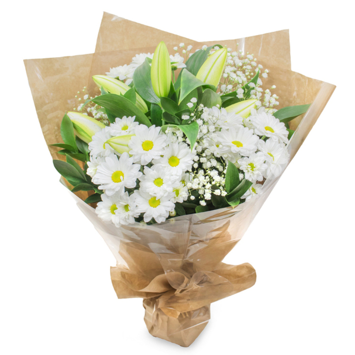 Against a bright white background, a serene bouquet of white and green flowers is shown upright, the composition radiating calm and refinement. The arrangement is dominated by numerous white daisy-like chrysanthemums, their petals fine and layered, forming rounded blossoms with soft yellow-green centres that act as gentle points of light throughout the bouquet. These flowers are arranged closely together, creating a plush, comforting texture reminiscent of a soft cushion placed in a peaceful Stanmore living room. Rising gracefully above and between the daisies, long lily buds stretch upward, their surfaces smooth and unblemished. Mostly a fresh, pale green, the buds fade into creamy white at the tips, hinting at the elegant blooms that will open gradually over the coming days. Threaded delicately among these primary flowers, tiny sprays of baby's breath scatter clusters of miniature white blossoms, softening the overall silhouette and lending a dreamy, ethereal quality. Encircling the bouquet, lustrous dark green foliage arcs outward, each leaf adding structure and supporting the contours of the hand-tied design. The stems are carefully gathered at the base and wrapped in earthy brown kraft paper, its textured surface gently creased and folded, imbuing the bouquet with a natural, artisanal character that feels at home in the quieter streets near Stanmore station or the avenues around the local parks. A clear cellophane layer surrounds the lower part of the arrangement, giving a subtle sheen and ensuring the bouquet arrives fresh and protected for local delivery. The overall effect is one of understated elegance and gentle comfort, making this design fitting for sympathy occasions, remembrance services, or any moment when a soft message of peace and support is needed.