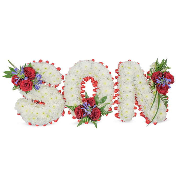 A solemn and lovingly crafted funeral tribute spells SON in large sculpted letters, every character formed from a compact sea of small white spray chrysanthemums that give each face a soft, cloudlike finish against a plain white background. The perimeter of each letter is outlined by a bright red satin ribbon, neatly pleated to form a scalloped edge that crisply separates the white floral field from the surrounding space and enhances the letters' three-dimensional presence. Thoughtful accent clusters add a classical touch: the S is accented at its upper left with several deep red roses paired with narrow, blue-purple spike flowers and abundant dark green foliage, the O receives a complementary cluster at its lower centre, and the N is ornamented on its upper right with a trailing arrangement of roses, blue spikes, and fern-like leaves. The combination of textures - velvety rose petals, feathery chrysanthemum heads, spiky blue accents and glossy leaves - creates visual rhythm and a meditative mood. The lighting is soft and even, allowing the colour contrast of pristine white and vivid red to communicate purity and love without ostentation. If placed near a funeral chapel by Stanmore Hill or alongside tributes at Bentley Priory memorials, this arrangement reads as a restrained, heartfelt message of remembrance. The composition demonstrates the careful touch of an experienced florist, offering both comfort and dignity where families gather to honour a beloved son.