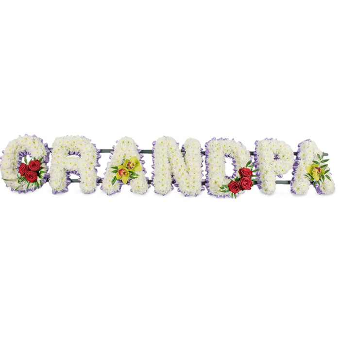 In this image, the word GRANDPA is lovingly spelled out in a horizontal line of floral lettering, each capital letter crafted from a dense layer of crisp white chrysanthemums that look almost like soft, ruffled snow. The petals overlap closely to form a smooth, cushioned effect, conveying gentleness and a sense of quiet comfort. Around the outer edge of every letter runs a thin band of pale lavender ribbon, the subtle hint of colour sharply defining the shape of the word while maintaining a soothing, understated palette suited to a funeral or memorial setting. Within the curved opening of the first G, three to four deep red roses rest among glossy green leaves, the bold crimson hue drawing the eye and symbolising deep love and gratitude. The third letter, A, is adorned with a small spray of yellow-green orchids, each blossom delicately veined and some shaded with russet tones in the centre, introducing a touch of exotic refinement. At the middle of the name, the rounded D contains a second cluster of red roses and foliage, mirroring the G and creating a sense of visual balance across the tribute. The final A on the right repeats the orchids, softly echoing their colour and shape. Discreet metal bars link the letters along the base, forming a single, cohesive arrangement ready to be placed on a stand in a church, crematorium, or cemetery serving Stanmore families and the surrounding HA7 area. The tribute feels both traditional and personal, offering a heartfelt farewell for a cherished grandfather whose presence shaped family gatherings, walks through Canons Park, and everyday life in the local community.