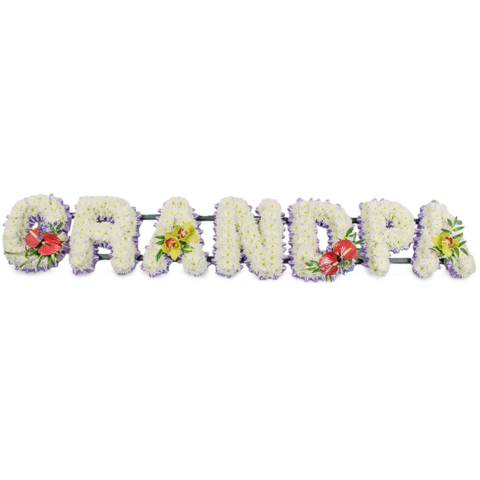 A long line of floral lettering spells GRANDPA in confident capitals, the entire tribute set against a plain, bright white background that highlights every petal. Each letter is shaped with precision and then densely covered with small, clean white chrysanthemums so that the word appears almost sculpted from flowers. The heads of the blooms are packed closely together, forming a plush, almost quilted texture that evokes comfort and purity. Their white petals catch the light subtly, giving the surface a soft sheen, as though the letters are gently glowing. A neat frill of light lavender ribbon runs around the base of each letter, just visible beneath the flowers, adding a faint violet edge that separates the shapes and brings calm, cool undertones to the tribute. Supporting bars, wrapped discreetly in dark green, hold the letters in a straight line, ready to be positioned in a Stanmore church, synagogue, or crematorium, perhaps overlooking the greenery towards Bentley Priory Nature Reserve. Bursts of colour are woven into the design with deliberate care: the 'G' is adorned with bold red anthuriums, their waxy, heart-shaped petals and pale spadices rising above glossy foliage to create a striking focal point. The first 'A' features an elegant spray of yellow-green orchids, each bloom delicate yet distinctive, emerging from lush green leaves. The 'D' repeats the rich anthuriums, mirroring the 'G' and bringing visual balance to the centre, while the final 'A' echoes the first with more fresh orchids in the same soft lime shade. It feels like the work of an experienced Stanmore florist who understands how to blend tradition, elegance, and personal sentiment, creating a tribute that quietly says thank you, Grandpa during a final farewell.