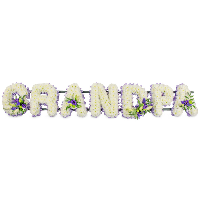 The photo features a heartfelt floral tribute spelling out GRANDPA in prominent block letters, lined up neatly in a row as though placed on a stand at a Stanmore memorial service. Each letter is generously padded with small, fresh white flowers, probably chrysanthemums or carnations, arranged shoulder to shoulder so that no gaps in colour or texture are visible. The petals are soft and rounded, creating a plush, uniform surface that radiates calm and reverence, much like the stillness you might feel stepping into a chapel near Stanmore Hill on a quiet morning. Into the surface of these white letters, the florist has tucked gentle accents of deep purple and lavender blooms, enhanced by touches of vibrant green foliage. These coloured clusters draw attention to particular areas: within the curve of the G, the centers of the As, and the bowls of the D and P, offering small but meaningful contrasts, like brief flashes of shared memories amid the steady presence of grief. All the letters rest on a discreet dark green frame, almost completely hidden by the flowers, which keeps the word aligned and allows it to be moved safely from the hearse to the chapel and then to the graveside. This kind of bespoke lettering piece is the sort of tribute a family in Stanmore might choose when they want a personal, visually clear way of honouring a grandfather at a funeral, whether the service is held locally or at a crematorium a short drive away. It communicates enduring love and respect, shaped with the attentive care of an experienced florist mindful of the emotions that surround a final farewell.