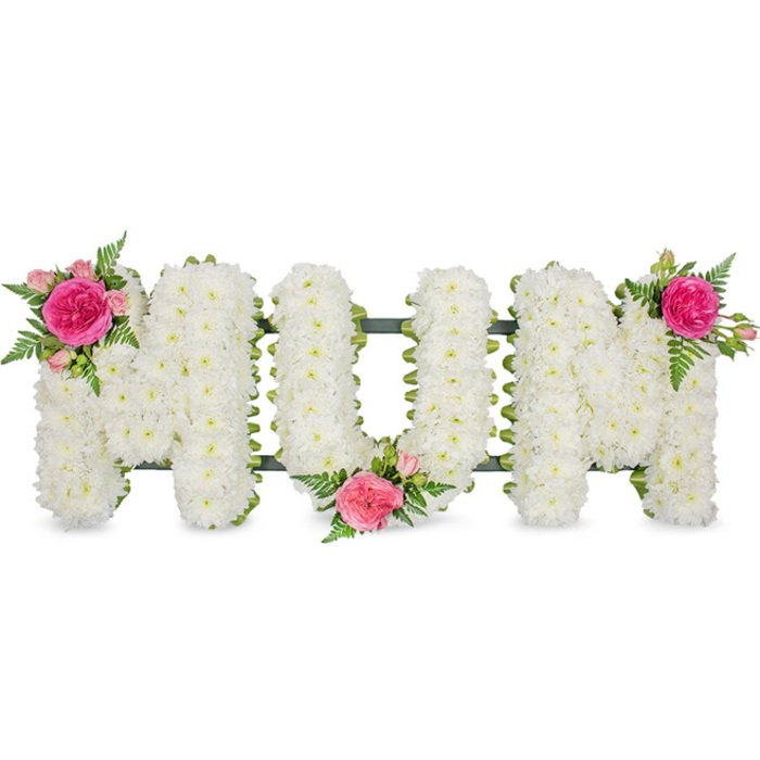 Against a clear white background, this image showcases a heartfelt floral tribute that spells out MOM in strong, upright block letters, the word instantly readable and emotionally resonant. The letters themselves are constructed on a dark green stand or frame, which can be subtly seen at the base, hinting at the sturdy mechanics that allow the arrangement to be displayed at a funeral service or graveside in and around Stanmore. Every visible surface of the letters is carpeted with small white chrysanthemum blooms, set so close together that no gaps can be seen between them. The petals form a plush, even layer, the cool white colour evoking a sense of peace, remembrance, and gentle farewell. This cushion-style effect softens the sharp edges of the lettering, giving the tribute a tender, comforting appearance. To individualise and brighten the design, three clusters of pink roses and greenery are artfully placed. The first cluster sits at the upper left of the initial M, where a bold fuchsia rose dominates, surrounded by lighter pink rosebuds and smaller heads that seem to be just unfolding, with arching fern fronds adding height and movement. A second cluster rests lower down between the circular O and the final M, anchoring the centre of the tribute and drawing the eye inward. The third cluster mirrors the first at the upper right of the last M, visually balancing the arrangement so the pink accents appear at three graceful points along the word. The finished piece suggests both love and dignity, the sort of memorial a family in Stanmore might choose to express their gratitude and affection for a mother who has passed, the fragrance of fresh roses mingling softly with the more delicate scent of chrysanthemums.