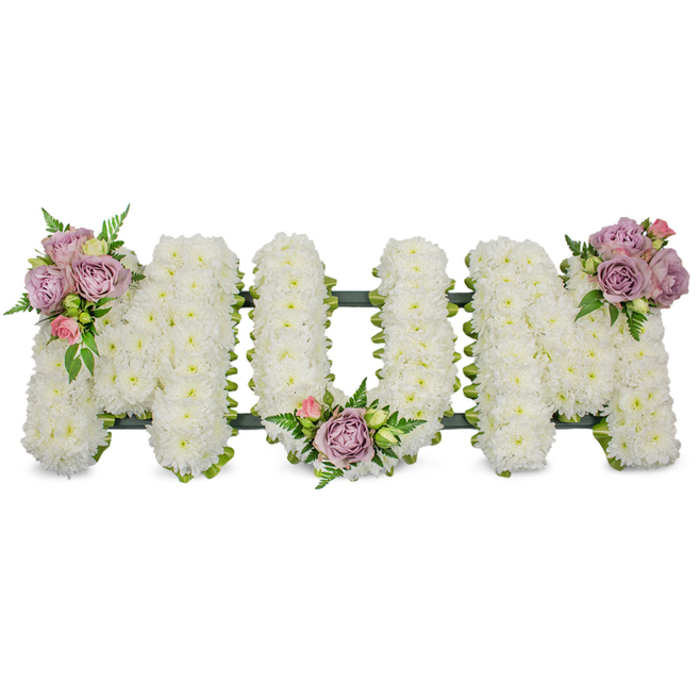 This elegant memorial composition reads clearly as the word MUM, each of the three capital letters densely clad in pristine white chrysanthemums so finely packed they appear as blankets of soft texture against a bright white backdrop. The chrysanthemums' compact sprays create a uniform, luminous surface that absorbs light gently, while their subtle scent contributes to an atmosphere of thoughtful quiet. Strategically placed for balance and sentiment, three small clusters of accent roses - mostly soft lavender with touches of pale pink buds - add a whisper of colour: one cluster crowns the upper left stroke of the opening M, another nestles within the inner curve of the central U, and the final grouping highlights the upper right arm of the closing M. Fresh green foliage, from feathery fern fronds to glossy leaves, weaves between these clusters, giving the piece fresh contrast and softening the hard edge of the letter forms. A dark green support frame, visible as a slim outline beneath the blooms, is likely wrapped in ribbon or moss to offer structural integrity without distracting from the flowers themselves. Seen in gentle, diffuse light - the kind we favour in our Stanmore studio during morning preparations - the arrangement conveys purity, respect and quiet consolation. It is intended for funeral services, memorial gatherings or graveside dedications, a bespoke expression of remembrance that balances traditional sympathy form with delicate, personal touches for families around Stanmore, Pinner and Harrow.