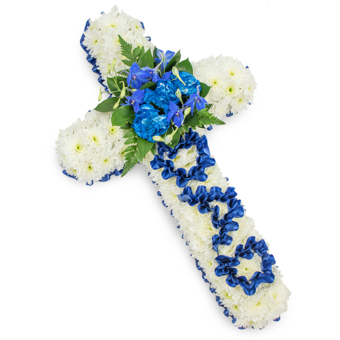 Set against a bright, uncluttered white backdrop, a beautifully composed funeral cross takes centre stage, radiating calm and reverence. The cross is entirely enrobed in small white spray chrysanthemums, placed so closely together that no gaps can be seen, forming a velvety, pillow-like surface. Each bloom contributes to a sense of purity and stillness, making the design particularly poignant for a father's farewell in or around Stanmore. Outlining the entire shape is a deep royal blue satin ribbon, folded and gently gathered so that it frames the white flowers with a defined, shimmering edge. The ribbon's rich colour and lustrous texture provide a dignified contrast, much like the formal yet welcoming atmosphere of local Stanmore churches and chapels. At the central intersection of the cross, a lush cluster of royal blue flowers draws the eye. Ruffled blue carnations dominate this focal spray, their layered petals adding volume and depth, while slender stems of blue delphinium or orchid-like blooms rise just above, introducing a touch of graceful height. Dark green fern fronds and broader foliage are interwoven among the blue flowers, softening the design and creating a natural, garden-like feel reminiscent of walks through Canons Park or Stanmore Country Park. Along the vertical arm of the cross, the word DAD is lovingly handcrafted from the same royal blue ribbon, each letter carefully formed in loops and curves that stand out clearly from the white chrysanthemum background. This sensitive, personalised detail gives the tribute emotional weight, suggesting cherished memories and lasting bonds. Overall, the piece feels substantial yet gentle, a fitting floral expression of respect, comfort, and remembrance for a beloved father in the Stanmore community.