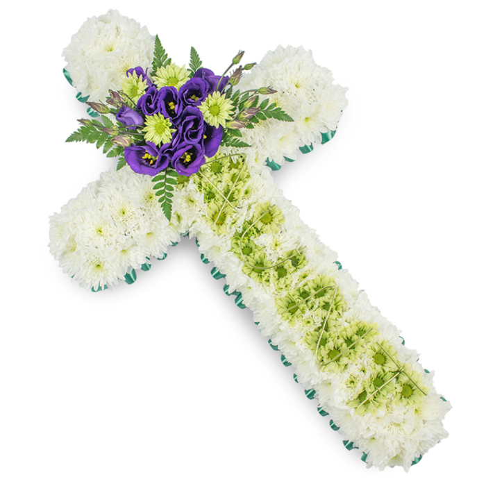 A beautifully composed floral cross, intended as a funeral or memorial tribute, is shown against a clean white backdrop, its soft colours and structured styling reminiscent of a quiet afternoon around Stanmore Hill. The main surface of the cross is completely covered with neatly arranged white chrysanthemums, their compact, feathery petals merging into a smooth, padded layer that feels calm and contemplative. Around the entire outline of the cross, a strong border of vivid green forms a crisp frame, crafted from ribbon or perhaps a tight collar of foliage, ensuring the traditional shape stands out clearly. Down the centre of the vertical arm, a band of lime green button chrysanthemums has been inset, the tiny, rounded blooms forming a raised, textured panel of fresh colour. Draped lightly over this green strip, fine white or pale green decorative wires cross over one another, creating a subtle lattice effect that introduces an element of delicate craftsmanship. At the exact spot where the vertical and horizontal arms meet, a striking cluster of deep purple lisianthus is arranged as the focal heart of the design. The lisianthus petals, velvety and gently ruffled, stand out beautifully against the white background of chrysanthemums. Interspersed with these rich purple blooms are bright lime green button chrysanthemums, while dark green fern fronds curve outward, adding depth and a soft, natural silhouette. The overall impression is one of quiet dignity and faith, making this floral cross an appropriate and meaningful tribute for a church service or graveside ceremony in Stanmore, carried with care by Flower Delivery Stanmore as a symbol of remembrance, sympathy, and spiritual comfort.