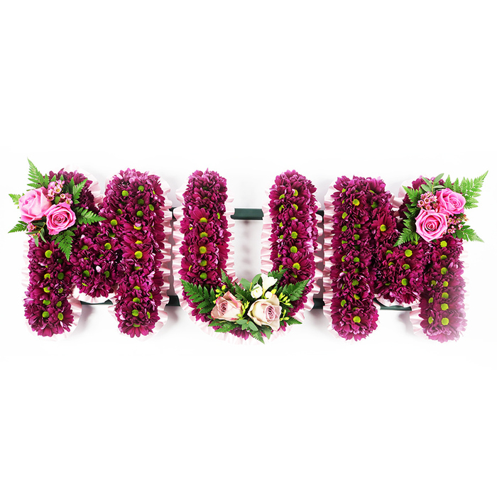 A large, bespoke floral arrangement depicting the word MUM in capital letters is displayed against a pure white background, giving the impression of a tribute ready to be placed at a Stanmore chapel, crematorium, or graveside. The three letters are formed from sturdy frames that are completely obscured by a dense covering of small spray chrysanthemums, predominantly in vivid fuchsia-purple and deep magenta shades. The blooms are set so close together that they form a smooth, cushion-like texture, with soft lime-green centres that dot the surface and provide a gentle, natural highlight. Running along the outer edges of each letter is a narrow band of pale pink ruffled ribbon, neatly pleated and fixed to follow every notch and curve, adding a delicate, dressmaker-like finish that softens the strong silhouettes. On the upper left of the first M, two larger, open pink roses are arranged amidst smaller rosebuds, their petals curling outward in layered spirals, accompanied by fine, feathery fern fronds that fan out slightly, giving the design movement and depth. At the base of the U, a small crescent of blush pink roses and creamy white, freesia-style flowers is cradled within the curve, backed by fresh, ferny greenery that seems just cut, like foliage gathered from one of Stanmore's green spaces. The second M reflects the first with a similar accent of bright pink roses and fern leaves placed high on its upper right edge, drawing the eye from one side of the tribute to the other. This MUM arrangement, created with chrysanthemums, roses, and lush foliage, is a classic, personalised funeral piece that conveys enduring love, profound respect, and cherished memories of a mother or grandmother.