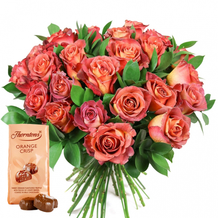 Beautifully showcased in the center of a pristine white background, this luxuriant bouquet of fresh roses draws attention with its soft gradation of warm hues-ranging from gentle peach and golden orange in the innermost petals to vibrant coral, fiery pinks, and deeper, almost ruby-toned outer rims. Each blossom exhibits subtle ombre and bicolor transitions, creating a visually compelling, richly textured floral sphere. Densely gathered, the roses are offset by abundant dark green foliage-likely ruscus or eucalyptus-which adds visual depth and brings a refreshing Stanmore greenery vibe to the arrangement. In the foreground, a classic Thorntons Orange Crisp chocolate pouch leans invitingly, its light cream cover highlighting the brand and name in bold, dark letters, while a stylized image of glossy chocolate truffles conjures the promise of a tangy-sweet indulgence. Immediately in front, two real truffles sit temptingly, their smooth surfaces reflecting the light. The bouquet's long stems fan neatly below the blooms, signalling freshness typical of local Stanmore deliveries. This carefully balanced arrangement of radiant flowers and artisan chocolates evokes a spirit of celebratory gifting-ideal for anniversaries, Valentine's, birthdays, or spontaneous acts of kindness to neighbours across Stanmore Village or Belmont. The image captures how locally curated gifts by Flower Delivery Stanmore bring together beauty and taste to create lasting memories.