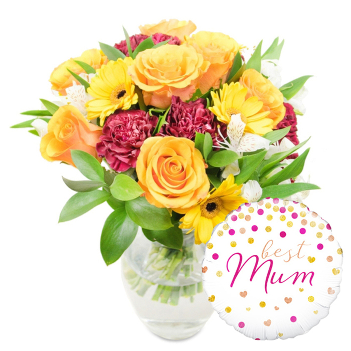 A bright and emotive floral arrangement shown against a crisp white field, set in a clear, unadorned glass vase that reveals the green stems and clear water inside, a mark of fresh conditioning. The bouquet's story is one of warm contrasts: several generous orange and golden-yellow roses form the focal point, their layered petals soft and tactile, while yellow gerbera daisies add cheerful, open faces with dark centres that anchor the light hues. Deep red to maroon carnations introduce a velvety, ruffled texture, their richer tones offering a romantic counterpoint to the sunlit roses. Interspersed white alstroemeria-slender, speckled and graceful-provide refined highlights and a faint floral perfume that mingles with the sweeter rose notes. Lush greenery, from broad glossy leaves to delicate filler sprigs, builds a living frame for the blooms and keeps the composition feeling abundant yet airy. Resting at the lower right, a round white foil balloon playfully overlaps the vase, patterned with scattered gold and fuchsia dots plus small heart motifs; its centre bears the flowing fuchsia inscription best Mum, turning the display into a tailored gift for a mother's celebration. Envision this as the kind of bouquet a Stanmore florist would place into a delivery box for same-day drop-off across the local neighbourhoods around Stanmore Common and Queensbury Road-a carefully balanced, joyful tribute meant to be both seen and savoured.