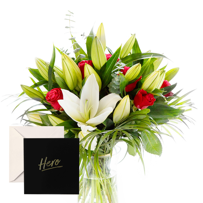 As a florist, there is joy in blending the bold with the serene, and this arrangement is a testament to that harmony. The white lilies drift at the heart of the bouquet, luminous and airy, their satin petals contrasting splendidly with the tactile, lush greenery that encircles them. Rich, ruby roses punctuate the design, each one a symbol of love and respect. The verdant leaves provide a cooling, almost forest-like backdrop, while unopened lily buds suggest anticipation and new beginnings. In this soft, natural light, the bouquet feels alive and uplifting, perfect for honouring someone's strength or celebrating a significant achievement. The accompanying Hero card makes this gesture feel both intimate and enduring. The arrangement would fit beautifully in Stanmore's living rooms, or at a doorstep near The Broadway, where it can offer a moment of quiet celebration. It is well suited to heartfelt thanks, sympathy, or recognition of leadership, and its classic palette ensures it remains cherished long after the initial moment. Delivered with care across Stanmore, the bouquet preserves fragrance and freshness, reflecting the attention of a local florist who understands the community's rhythms.