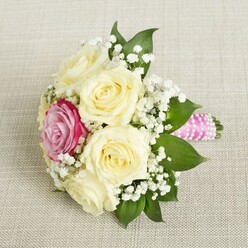 Envision stepping into a sunlit Stanmore wedding venue, where a bouquet awaits, reminiscent of early morning calm and joyful promise. The base is comprised of five to six creamy, ivory roses, delicately arranged with each petal displaying natural curves and a subtle, almost glowing sheen. Nestled among them is a lone magenta-pink rose, its vibrant color the heartbeat of the bouquet, providing a contemporary touch amid the classic cream palette. White clouds of baby's breath hover throughout, lending a sense of purity and softness, while lush, deep green foliage recalls Stanmore's leafy avenues and tranquil gardens. The stems are artfully bundled and bound by a smooth pink satin ribbon, completed with a spiral of glistening pearls-a modern take on timeless bridal elegance. Each detail is illuminated by diffused daylight, highlighting the intricate textures and imparting a feeling of expectation and hope. The bouquet rests on neutral-toned linen, its gentle texture reflecting both local style and the thoughtful hands of an experienced Stanmore florist. Ideal for weddings, bridesmaid ensembles, or simply as an expression of love, this bouquet exudes sincerity and exquisite craftsmanship rooted in the community's celebratory spirit.