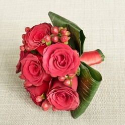 An elegant bouquet of rich red roses and berries lies on a light beige, finely textured fabric, as if just set down on a dining table in a Stanmore home prepared for a celebration. At the centre, several large roses open generously, their velvety petals unfolding from tightly furled hearts into soft spirals of crimson and deep ruby, creating a sense of intimacy and quiet drama. Interlaced between the blooms are delicate sprays of round Hypericum berries in shades of flushed red and warm rose, their smooth, bead-like forms adding an almost jewel-like detail. Surrounding the flowers, broad, glossy green leaves are artfully curved and layered, forming a natural collar that cradles the bouquet and adds structure, like a tailored frame around a cherished picture. A sleek red satin ribbon is wrapped firmly around the stems, visible to one side, its subtle sheen catching the light and finishing the design with a refined flourish. The overall lighting is soft and balanced, with no harsh glares, allowing the rich reds and deep greens to glow gently against the neutral background. This arrangement feels perfect for a bridesmaid walking through Stanmore's quiet residential streets to a local wedding venue, or for a heartfelt anniversary surprise delivered across Canons Park and the surrounding HA7 area. It carries the scent of fresh greenery and the romantic promise of roses, capturing a mood of joy, gratitude, and shared moments that linger long after the flowers are placed in a vase.