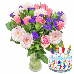 Batheed in gentle morning light, this birthday bouquet presents itself as an eloquent mix of soft pinks and lively purples arranged with careful, local expertise. The centerpiece is a generous cluster of pink roses, each petal layered like silk and graduating from pale blush at the outer edges to a more saturated pink toward the center, suggesting tenderness and celebration. Surrounding them, pale pink Gerbera daisies open wide, their round faces and cream-yellow discs bringing cheer and a hint of vintage charm. Threaded throughout are dense sprays of vivid purple statice or limonium, providing crisp texture and a jewel-like contrast against the roses and daisies. Small white filler blooms and abundant glossy green leaves give the arrangement volume and a natural, freshly-cut feel. The bouquet is displayed in a clear glass vase with visible stems and fresh water, a stylistic choice that emphasizes freshness and straightforward beauty. To the right, a white cake-shaped Mylar balloon decorated with blue icing, colorful sprinkles, and four multicolored candles reads Happy Birthday in playful letters; a tiny KALEIDOSCOPE mark sits at its foot. As a Stanmore florist I picture this arrangement arriving on a sunny morning to a home near Stanmore Hill or Belmont Circle, the gentle fragrance of roses and greens filling a kitchen while neighbours pass by. Flower Delivery Stanmore offers similarly styled celebratory designs for local delivery, and this particular floral pairing is ideal when you want a refined bouquet with a fun, modern accent for birthdays and intimate gatherings in and around our neighbourhood.
