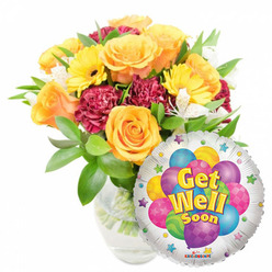 An encouraging, sunlit "Get Well Soon" ensemble arranged to lift spirits: a full, rounded bouquet in a clear glass vase paired with a round silver Mylar balloon bearing a playful printed message. Large, opening roses in soft orange and deep sunflower yellow create the central focus, their layered petals suggesting softness and a light citrus scent. Bright yellow gerbera daisies punctuate the bouquet with cheerful faces, while deep maroon carnations provide a velvet contrast and tactile richness. Fleeting clusters of white alstroemeria peek from between the larger blooms, offering delicate lines and a whisper of contrast against the richer tones. Fresh green foliage-shiny, turgid leaves and feathery backing stems-enfolds the flowers and conveys a freshly made, just-watered warmth; the clear vase exposes clean stems and water, a sign of careful floral conditioning for lasting freshness. The balloon, positioned slightly in front of the lower right, has a reflective silver field decorated with colorful cartoon-style balloons in blue, purple, lime, pink and yellow-some with stripes or polka dots-and bold yellow-and-blue lettering that reads "Get Well Soon," edged by playful starbursts; the tiny "KALEIDOSCOPE" logo sits at the bottom rim. As a local florist familiar with Stanmore High Street and the quiet mornings around Stanmore Common, I see this as a bedside cheer-a thoughtful gesture for someone recovering, ready for same-day delivery across NW7 when you need a bright, comforting pick-me-up from Flower Delivery Stanmore.