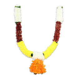This U-shaped ceremonial garland, photographed against stark white to show every detail, reads like a small study in traditional colour and craft - the kind we make for doorways and altars in and around Stanmore. Beginning at each upper arm, compact clusters of soft, creamy-white florets resemble miniature chrysanthemums; under studio light they appear almost pillowy, offering a quiet, ceremonial calm. Directly beneath, a rich band of reddish-brown elements provides a tactile contrast: these flattened, textured pieces suggest layered petals or preserved leaf shapes that introduce depth and warmth. The curve broadens into a vivid yellow section formed of tightly packed marigold-like pom-poms, their bright golden tones creating the familiar festive sweep of the "U." Small green accents-leaf-like knots or ribbons-mark the joins and lend a subtle botanical punctuation.

Hanging from the lowest point, a voluminous orange pendant commands the composition. Its ruffled, multi-layered petals create a rounded, buoyant form that reads as both focal ornament and symbolic offering. The materials feel silky yet substantial, chosen for longevity so families can reuse the garland for Diwali, Ganesh Chaturthi, weddings, or temple decoration. As a Stanmore florist I picture this piece brightening an entrance near Canons Park or gracing a home on the Broadway; Flower Delivery Stanmore can prepare similar styles for local delivery. The overall effect is celebratory and reverent-traditional hues and confident construction that hold their festival spirit season after season.
