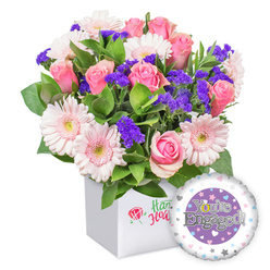 This joyful bouquet exudes balanced elegance and layered texture, crafted with a deft hand and a keen eye for color. Pink roses, their petals unfurling in soft, creamy spirals, take center stage, complemented by moonlit pink gerberas that bring a light, airy rhythm to the arrangement. Interspersed are clusters of deep purple statice, lending vibrant pops of color that feel like secrets tucked among the blooms. The bouquet reads lush and whimsical, with generous green foliage spilling around the stems to create a garden-fresh, expansive look. Encased in a snowy white square box that keeps the composition clean and contemporary, the display is anchored by a front logo-a red rose icon paired with green script-signalling quality without shouting. To the lower right, a round foil balloon in pastel tones completes the celebration, its purple center bearing "You're Engaged!" in silver lettering, while the golden "O" in "You're" adds a touch of luxury. A ring of pastel hearts and tiny silver stars around the balloon's edge reinforces the joyous mood. Ideal as an engagement gift, this arrangement feels crafted for happiness and bright beginnings, available for same-day delivery across Stanmore and the surrounding NW London pockets by Flower Delivery Stanmore.