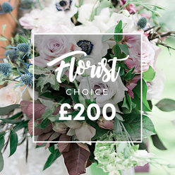 Presented by Flower Delivery Stanmore, this elegant Florist Choice bouquet dominates the frame, its center crowned by a soft white overlay reading Florist CHOICE ?200. The arrangement exudes refined luxury, the kind of design a Stanmore client would treasure for a wedding, anniversary, or a thoughtful celebration. Delicate light pink garden roses stand open and radiant, mingling with creamy white and pale lavender-grey roses, while white anemones with their near-black centers add dramatic focus. Subtly purple-grey roses introduce a contemporary edge, and spiky blue eryngium thistles break the softness with crisp architecture and cool color. Lush greenery-eucalyptus-like leaves and deep burgundy or plum foliage-weaves through the bouquet, creating texture, depth, and a sense of leafy movement. The composition feels natural and substantial, a bespoke piece crafted with evident care by a local studio serving Stanmore, Canons Park, and surrounding NW London communities. In the soft background, gentle outdoor light enhances every petal and vein, inviting the viewer to imagine this bouquet on a wedding altar or a celebratory dining table. For delivery, this elegant design is available from Flower Delivery Stanmore with dependable same-day service across Stanmore and nearby neighbourhoods, ensuring a luxurious gift arrives fresh and fragrant at ?200.
