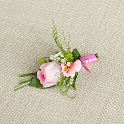 Capturing the essence of a joyful occasion in Stanmore, this artful boutonniere rests lightly on a natural, woven beige fabric background, redolent of the community's relaxed yet refined spirit. The centrepiece, a pastel rose blushing from a richer pink heart to gentle outer edges, is a classic flourish, its tightly-wound petals suggesting freshness and anticipation. Nestled beside it, a soft alstroemeria in hues of pink and peach reveals sunny yellow streaks and dark, intriguing markings, evoking the delicate patterns admired at Stanmore's artisan markets. Flurries of delicate baby's breath and pint-sized green mums add textured volume and pops of cheerful energy, while the bouquet's verdant green backdrop recalls the sweeping expanses of Canons Park. Slender, dark green blades and feathery sprigs arc gracefully upwards, balanced by sturdy, deep green leaves folded with precision at the base. The design is crowned with a lush, dark green ribbon leaf enveloping the stems, all secured with a vibrant fuchsia pink satin bow-a whimsical finishing touch reminiscent of festive moments at Stanmore's community celebrations. The soft lighting enhances every detail, inviting the viewer to imagine the subtle scent, gentle textures, and celebratory promise this boutonniere brings, making it an ideal adornment for elegant occasions from weddings to graduations throughout Stanmore.