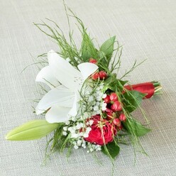 In this thoughtfully designed bouquet, the artistry of a seasoned Stanmore florist comes alive in a palette of red, white, and green, resting atop a textured backdrop that conjures the warmth of Stanmore's local venues. Dominating the arrangement, a radiant star-like white lily unfurls its petals-crisp and silky to the touch, delicately overlayed with fine reddish-brown speckles and golden anthers at its center. Closely nestled, a lush deep red rose-its petals softly curled inward-embodies classic romance and devotion. Intertwined amid the focal blooms, clusters of glossy red berries evoke a festive spirit, recalling joyous gatherings and celebrations often held in Stanmore's leafy neighborhoods. Accents of feathery baby's breath infuse a gentle, cloud-like texture, gracefully softening the composition, while fresh green fronds and smooth, broad leaves cradle the bouquet, adding both volume and verdant vitality reminiscent of the gardens at Canons Park. At the side, a slender green lily bud suggests a forthcoming bloom, symbolizing hope and new beginnings. The arrangement is elegantly cinched at its base by a vivid red satin ribbon, reflecting the bouquet's romantic and celebratory tones. This refined piece serves as an exquisite bridesmaid bouquet or heartfelt gift, imbuing every Stanmore occasion with freshness, elegance, and the expert touch of a true local florist.