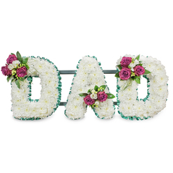Presented against a plain white background, this handcrafted memorial spells DAD in bold, three-dimensional letters, each letter densely covered in small, immaculate white chrysanthemums that form a soft, cloud-like surface. The white blooms are closely clustered to create seamless contours; their tiny petals catch light in a way that reads as purity and calm. An emerald-green, pleated ribbon neatly outlines each letter's edges-both outer and interior-introducing a cool, dignified contrast that frames the composition and gives the wording a defined silhouette. Behind the lettering a dark green or slate-grey support bar runs horizontally, suggesting the sturdy stand used for wake or service displays.

Deliberate clusters of deep magenta roses and small white freesias are placed for balanced emphasis: a bouquet on the upper left curve of the first D, another tucked into the lower centre V of the A, and the last cluster on the upper right of the final D. The roses' deep colour and the freesias' subtle fragrance create a gentle harmony, while rich green foliage adds depth and a grounding tone. As a Stanmore florist I picture this tribute quietly appropriate for services at St. Luke's or for a graveside near Canons Park; it carries a traditional sympathy message told with personal warmth. Flower Delivery Stanmore prepares pieces like this with careful attention to texture, scent and proportion, mindful of local families seeking a heartfelt farewell.