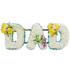 A deeply personal memorial arrangement that spells DAD in three freestanding block letters, each letter meticulously covered in a dense blanket of small, pristine white spray chrysanthemums that create a velvety, uniform surface. The letters are trimmed with a ruffled dark-green satin ribbon, which gives a tailored edge to the white blooms, while dark green metal bars behind the letters connect them into a single, stable display. On the left D, a bright cluster of yellow roses-about three or four blooms-sits on the upper curve, surrounded by tiny white filler flowers such as freesias or gypsophila and fresh greens; two long, slender bare stems extend diagonally from that cluster toward the middle, drawing the eye inward. The central A is anchored with an elegant accent on its lower left diagonal: two deep purple or burgundy calla lilies stand in sophisticated contrast to the white chrysanthemums, their smooth, trumpet-like forms surrounded by small white accents and glossy foliage. The right D mirrors the left, bearing a matching yellow-rose cluster on its upper right curve. Presented against a clean white background and photographed in soft, even lighting, this tribute reads as calm and reverent-white for peace, yellow for friendship and fond memory, purple for devotion. As a local Stanmore creation-suitable for services near Stanmore tube station, Canons Park, or family gatherings on Stanmore High Street-this piece may be arranged for careful delivery across Stanmore and neighbouring Harrow. The scented impression is subtle and fresh; the craftsmanship speaks of an experienced hand arranging each bloom with intention and respect.