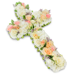 This photograph showcases a sizeable Christian cross crafted entirely from fresh flowers, resting against a clean, bright white background that enhances its gentle colour palette. The cross is heavily adorned with a soothing mixture of white and cream-toned blooms, including tightly clustered roses, fluffy hydrangea heads, and smaller filler flowers that together form a thick, luxurious cushion of petals. Woven into this soft white canvas are blush pink and pale peach roses, arranged in small clusters along the vertical stem and crossbar, bringing subtle warmth and dimension to the design. Their open petals, with shades that fade from soft apricot at the centre to delicate pink at the edges, evoke a feeling of tenderness and quiet grace. Here and there, tiny sprigs of lavender or light purple filler flowers peek from between the larger blossoms, like gentle whispers of colour that guide the eye across the piece. Fine, fresh green foliage outlines sections of the cross, defining its shape without overpowering the pastel theme. The result is an arrangement that looks both full and airy, as if it could have been prepared for a memorial service or funeral in Stanmore, perhaps for a ceremony near Canons Park or along Stanmore Hill. The bright, even lighting brings out every curve and crease of the petals, making their textures almost tangible. This floral cross feels like a heartfelt tribute, a carefully crafted symbol of remembrance, hope, and spiritual comfort, created to accompany a loved one's final journey with dignity and beauty.