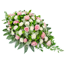 This serene floral tribute is shown against a clear white backdrop, highlighting its elegant, elongated teardrop curve from left to right. The design rests on a gentle gradation of colour, moving from clusters of soft pink roses to pockets of pure white carnations. Each pink rose is carefully placed, with petals unfurling in soft spirals, some still shy and cup-shaped, others fully open to reveal a layered heart in warm blush and rose-pink tones. The white carnations and spray carnations are tucked among the roses, their finely frilled petals resembling little tufts of foam or cloud, adding fullness and a sense of softness. Beneath and around the flowers, lush greenery frames the composition. There are broad, glossy dark green leaves providing structure and a reassuring solidity, while rounded eucalyptus leaves in a muted, silvery green thread between the blooms, bringing a cooler tone and a subtle suggestion of fresh fragrance. From the tapered right tip of the spray, slender trailing stems of dark green ruscus extend gracefully, enhancing the impression of flow and movement. The overall mood is calm, considered, and respectful, a floral arrangement that speaks gently of remembrance and farewell. It is the kind of tribute families in Stanmore might choose for a service at a local church off Marsh Lane or a quiet goodbye near Stanmore Country Park, reflecting both care in its craftsmanship and tenderness in its colour and shape, offering solace at a time when emotions run deep.