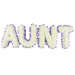 As a florist shaping remembrance for local families, I describe a lovingly made floral wording that reads 'AUNT' in bold capital letters, each formed from tightly packed white spray chrysanthemums. The blooms present as soft, ruffled domes-small petals layered like fine lace-while occasional pale-yellow eyes bring a natural, delicate warmth to the otherwise pure white surface. Around each letter, a rich purple satin ribbon has been thoughtfully pleated and ruffled, its satiny sheen catching the light and defining every corner, lending both contrast and a sense of finish. Gentle grey shadows under each letter indicate the raised frames and provide a quiet sense of depth against the clean white backdrop. There is a faint, fresh scent: green, slightly sweet and reassuring, underlining the careful freshness of the flowers. This tribute is crafted to convey dignified affection and personal memory, the sort of arrangement we prepare for intimate services at local chapels or for families leaving a last floral message at Bentley Priory or Stanmore Park. At Flower Delivery Stanmore, we handle these commissions with the same attention to structure and sentiment-securing blooms for longevity and arranging ribbon so it sits like a supportive cuff around each letter. The overall effect is gracious and consoling, a tactile and visual ode to a beloved aunt that stands as both an emblem of loss and a celebration of a life that touched a neighbourhood.