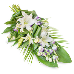 This image shows a thoughtfully designed sympathy arrangement set against a clear white backdrop, the spray arranged in an elegant teardrop that flows from a full top section to a delicate point below. The main feature is a series of white oriental lilies, some fully open with graceful, trumpet-shaped blooms and softly curved petals, others still in bud, their ivory casings suggesting blossoms that will gradually open after the ceremony. Interwoven among the lilies are clusters of lisianthus flowers, each small bloom white at the centre and edged in the softest lavender or pale purple, with fine veins adding texture and interest. Closed buds and half-open lisianthus blooms create a sense of gentle rhythm along the length of the piece. Around the flowers, an abundance of green foliage provides structure and contrast. Broad, glossy leaves lend weight at the base, while long, slender fronds sweep out from the side to draw the eye along the arrangement's diagonal line. Some leaves are carefully rolled and folded, lending a modern, sculpted touch to the natural composition. The spray has the quiet poise of an arrangement prepared in Stanmore for a farewell at a local church, synagogue, or crematorium, perhaps arriving by hearse along Honeypot Lane or past Stanmore Country Park. Its restrained palette of white, green, and faint lavender conveys purity, comfort, and respect, making it suitable for placing on a casket, beside a memorial photograph, or near a book of condolence during services in and around Stanmore.