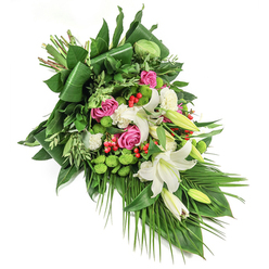 Reflecting the serene atmosphere of Stanmore, this elegant funeral spray is meticulously arranged to cascade diagonally, creating a visual journey from the top left to bottom right of a snowy white background. The bouquet's focal point is the immaculate display of white lilies-some in full bloom, revealing golden anthers, while others remain closed, signifying remembrance and the tenderness of an ongoing bond. Amid these, deep pink roses lend soulful warmth, their delicate petals gracefully opening to the light, evoking the nurturing communities along Uxbridge Road or near Stanmore Park. White spray carnations enhance the arrangement's plush texture, while rounded lime-green santini chrysanthemums provide playful, moss-like pops that lift the mood and offer a contemporary edge. Small, fiery red hypericum berries bring forth flashes of colour and joy, harmonising with the bouquet's abundant and varied foliage, which includes broad, glossy leaves folded and layered for structure, as well as lighter sprigs and lengthy palm fronds swaying gently downward. The interplay of light and texture across the arrangement creates a tranquil, comforting effect, ideal for offering condolences and quiet support to families in Stanmore. Crafted with empathy and artistry, and available for same-day delivery, this distinctive spray stands as an enduring symbol of tribute and solace.
