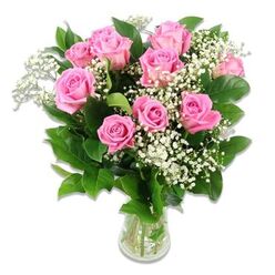 A refined and gentle bouquet of pink roses and baby's breath is arranged in a clear glass vase, set against a bright white background that mirrors the quiet, airy light often seen in Stanmore homes on a clear morning. The arrangement forms a rounded, abundant shape, with approximately ten to twelve pink roses at its core. Each rose displays layers of smooth, velvety petals that transition from a delicate, baby-soft pink around the edges to a slightly deeper, more saturated rosy hue as they spiral into the centre. Some blooms are fully open, wide and romantic, while others remain semi-closed, giving the bouquet a sense of movement and natural progression, much like watching a newborn grow day by day. Fine, branching stems of white Gypsophila, or baby's breath, are interlaced among the roses, their tiny star-shaped flowers forming fluffy, cloud-like clusters that lend an airy, weightless quality to the composition. Dark green foliage frames the blossoms, the leaves structured and slightly glossy, providing a strong contrast that helps the pink and white tones glow. The flowers are gathered neatly into a clear, cylindrical glass vase, partially filled with water in which the straight, green stems can be seen, emphasizing their freshness and careful preparation. The lighting is bright yet soft, with minimal shadow, so every detail of petal, leaf, and glass is visible, while subtle reflections play across the vase. This classic, pastel-toned bouquet feels ideal as a baby girl gift delivered across Stanmore, from family homes near Bentley Priory Nature Reserve to quiet streets off The Broadway, offering a tender, welcoming touch of beauty.