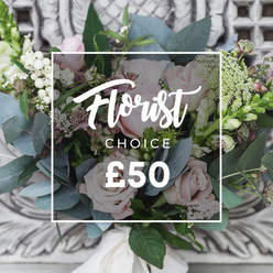 There's an easy, cultivated calm to this bouquet, as if gathered from an English cutting garden and tied with quiet intent. Soft blush roses form the rounded heart of the arrangement, their layered petals offering warmth and a gentle fragrance that pairs with the cooling scent of silvery eucalyptus leaves fanning out like muted sea glass. Bright white, pearl-like berries punctuate the soft palette, set against delicate sprays of tiny white filler blooms that provide an airy, lace-like texture. Deeper pink and burgundy accents sit low and shadowed, creating pockets of richness that make the pale roses feel even softer by comparison, while taller, slender flower spikes emerging at the sides add subtle height and a graceful silhouette. The stems are bound with a cream satin ribbon, finished by hand and left intentionally loose to preserve that freshly-cut, rustic-chic look. Photographed in soft daylight with an out-of-focus, ornate plaster background, the arrangement radiates an intimate, comforting energy-perfect for welcoming a new home near Stanmore Broadway, sending gentle well wishes, or marking a quiet milestone. An experienced florist would note the pleasing tactile contrasts here: velvet petals against waxy greens and the slight, reedy crunch of berries. The bouquet is a study in restraint and texture, designed to feel personal and thoughtfully curated rather than overly formal.