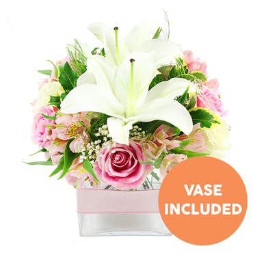 An artfully composed bouquet of white and pink flowers stands out against a pristine white background, captured with a clarity that highlights every petal and leaf, as though arranged on a polished table in a Stanmore kitchen flooded with light. Two prominent white Oriental lilies form the visual centre, their graceful petals folding back to reveal rich reddish-brown stamens that provide depth and contrast. Around these lilies, a ring of soft pink roses is nestled tightly; some are still curled in compact buds, others have opened into full, rosette-like blooms with layered petals that evoke a sense of romance and gentle celebration. Intertwined with the roses are stems of pink and white alstroemeria, with slender petals dusted in subtle yellow and fine markings, bringing movement and a touch of intricate detail. Wisps of white baby's breath intermingle throughout, giving the arrangement a light, cloud-like veil that softens the structure. Fresh greenery in varying shapes-from smooth, robust leaves to more delicate, feathery foliage-surrounds the blossoms, echoing the leafy calm of Canons Park and adding natural fullness. The bouquet sits neatly within a low, square clear glass vase, through which the green stems are clearly visible in the water, conveying a feeling of crisp freshness. A pale pink satin ribbon is wrapped horizontally around the middle of the vase, a simple yet elegant flourish that suggests a carefully prepared gift. In the lower right portion of the image, a round orange graphic displays the words VASE INCLUDED in bold white capital letters, clearly indicating that the container accompanies the flowers. The arrangement feels composed yet inviting, perfect for same-day delivery around Stanmore to mark an anniversary, thank a host, or bring quiet joy to a coffee table or bedside.