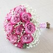 Resting against a soft, off-white linen background, this hand-crafted bouquet brims with the quiet elegance favoured in Stanmore's family gatherings and refined celebrations. The star of the composition is the dozen two-tone roses, their petals unfolding in gentle gradations from pale lavender-pink at the center to deep magenta and fuchsia at the outermost tips. Their rich colour is strikingly offset by delicate, white baby's breath, whose tiny, cloud-like flowers envelop the blooms with airy softness. Bound together by a glimmering pale pink ribbon, the stems are further enhanced by a spiral of tiny pearl beads, lending the bouquet a romantic, tactile charm reminiscent of wedding finery often seen at Stanmore Place or Bentley Priory. It lies gracefully across the neutral surface, the natural stem ends peeking below the ribbon, affirming the bouquet's freshness. The soft, balanced lighting highlights each petal and sprig, while the overall effect is one of optimism, love, and enduring joy-a visual tribute to special days celebrated in Stanmore's inviting neighbourhoods.