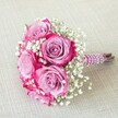 This vibrant, tightly arranged bouquet-ideal for weddings or milestone celebrations in Stanmore-features five lavish pink roses, each unfurling petals that transition dramatically from delicate lavender at the centre to bold fuchsia and magenta at the outer edges. Interspersed are airy clusters of white baby's breath, adding a gentle lightness and playful movement. The rounded bouquet exudes freshness, its stems tidily wrapped in a regal, subtly shimmering pink ribbon, the handle further enhanced by winding strands of small, lustrous white pearls. Natural green stems peek from beneath, adding a hint of rustic charm. The bouquet rests diagonally on a soft, off-white linen cloth, the quiet neutral tones letting the rich colours and intricate pearl detailing shine. Radiating joy and refined craftsmanship, this arrangement symbolises love and celebration-making it a perfect choice for weddings, bridal parties, or special occasions throughout Stanmore, and reflecting the expertise and personal touches provided by Flower Delivery Stanmore.