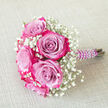 This small, hand-tied bouquet is captured resting on a pale beige, lightly textured fabric that feels like fine linen, creating a neutral canvas for its rich colours. At its centre, several lush bi-colour roses are clustered closely, their petals unfolding in smooth, velvety curves. Each rose begins with a soft lavender or light purple inner tone, then transitions toward the outer edges into intense fuchsia and magenta pink, producing a captivating gradient that draws the eye to every ruffle and fold. Interlaced with these statement blooms are plentiful sprigs of white baby's breath, their minuscule blossoms gathered in airy clusters that resemble tiny clouds, lending the bouquet a sense of lightness and tradition. The florist has gathered the stems with care, then wrapped them in deep purple satin ribbon, which appears sleek and satiny under the light. Over this ribbon, a delicate strand of white faux pearls spirals down the handle, each bead catching subtle highlights, adding an air of sophistication and bridal charm. Positioned diagonally so that the handle points to the right, the bouquet seems poised to be lifted for wedding photos in Stanmore Country Park or carried into a ceremony at a local synagogue or church. It feels intimate and refined, an ideal choice for a bridesmaid's bouquet, a prom posy, or a special-occasion accessory, crafted by a Stanmore florist familiar with the area's elegant celebrations, tree-lined avenues, and family gatherings that call for flowers with both personality and poise.