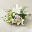 Resting on a soft, textured canvas akin to those found in Stanmore's elegant homes, this radiant bouquet combines classic wedding beauty with local charm. Towering white Oriental lilies stand as the focal point, each trumpet-shaped bloom unrolling majestic, luminous petals. Their vivid yellow anthers and delicate spots draw the eye, echoing the vibrancy of blossoming gardens along Uxbridge Road. Nestled among these, white Lisianthus blooms edged in dramatic purple provide texture and a painterly accent, as though plucked from Stanmore's countryside borders. A refreshing array of foliage - from glossy, broad leaves to fine, cascading ferns - wraps the bouquet in a natural embrace. Slim purple spires, likely Veronica, rise playfully above, while wispy baby's breath brings a cloud-like veil of softness. The bouquet is bound with silken white ribbon and arranged with care, its stems visible and neatly aligned. Under gentle daylight, the details shine: petals gleam, greens look dewy, and every nuance is elevated, offering an arrangement of serenity and sophisticated celebration. Suitable for bridal parties, romantic anniversaries, or refined occasions across Stanmore, this bouquet is a heartfelt reflection of the area's warmth and beauty, expertly crafted by Flower Delivery Stanmore.