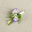 A delicately crafted wedding boutonniere rests on a softly textured light beige linen cloth, its neutral backdrop allowing every petal and ribbon to stand out with quiet elegance. At the heart of the design are two white lisianthus blooms, their petals gently ruffled and finely edged in a deep, velvety purple that creates a graceful halo of colour. Close beside them sit airy clusters of tiny white filler flowers, similar to baby's breath, adding a cloud-like softness and a sense of lightness to the small arrangement. Threading upward, a slim spike of tightly packed, bell-shaped muscari flowers in rich grape-purple introduces depth and a touch of whimsical texture, like something gathered from the borders of Bentley Priory Nature Reserve in Stanmore. Fine, feathery greenery, reminiscent of asparagus fern, fans out around the flowers, its fresh green tones and delicate fronds giving the buttonhole a natural, garden-picked charm. Two pale green unopened buds peek from the design, suggesting new beginnings and the unfolding of the day ahead. The stems are neatly aligned and wrapped in a crisp white satin ribbon, smoothed carefully and finished with a tiny, tidy bow, clearly prepared to be pinned securely to a lapel. The lighting is soft and even, emphasising the clean whites, rich purples, and fresh greens without harsh shadows, evoking an atmosphere of calm anticipation. This boutonniere feels perfectly suited to a groom or groomsman heading to a ceremony in one of Stanmore's local churches or registry offices, capturing the feeling of early-morning preparation and thoughtful detail that defines a carefully planned celebration.