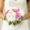 In this photograph, the bridal bouquet brings to mind the peaceful stillness of Stanmore's leafy streets on a bright, sunlit morning. Generous creamy peonies form the core of the design, their satiny petals slowly unfurling in soft ivory tones that hint at the palest blush near the centre. They have a natural, effortless beauty, like flowers that have just opened in a sheltered corner of a garden near Canons Park. Surrounding the peonies, roses in subtle dusty pink and soft violet shades offer a gentle warmth, their closely packed heads adding movement and subtle colour shifts throughout the arrangement. Wisps of gypsophila peek from between the larger blooms, their delicate, cloud-like clusters echoing classic bridal traditions while introducing airiness and light. Rich green leaves, smooth and slightly glossy, embrace the composition like a protective cocoon, making the pastel hues stand out with greater softness and depth. The bouquet is tightly gathered by hand, the stems aligned and likely bound with ribbon, creating a neat, compact shape that feels intimate and personal-perfect for an understated yet elegant wedding in Stanmore or along the quiet roads of Harrow Weald. The lighting is gentle and natural, casting a soft glow across the petals so that each flower seems freshly cut and full of life. The whole arrangement conveys tranquility, harmony, and a calm sense of celebration, as though every bloom has been placed with intention to reflect the couple's quiet joy, enduring love, and the serene beauty of their special day in this North West London suburb.