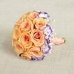 Embodying the elegance found along Stanmore's tree-lined avenues, this round bridal bouquet is artfully displayed against a gentle, textured beige fabric. The focal point is a domed mass of tightly nestled peach and soft orange roses, their plump blooms softly glowing like the first light over Stanmore Hill. Alongside, ruffled white lisianthus with rich purple margins add an exuberant twist and visual depth. Throughout, airy sprays of baby's breath offer a hint of movement and a delicate contrast, reminiscent of clouds drifting over Bernays Gardens. The stems are bested together and wrapped in a smooth peach satin ribbon-its tactile warmth mirroring the bouquet's fresh, springlike feel-while a strand of luminous pearls whirls around the handle for a refined, classic accent. Every element has been curated with the local expertise of Stanmore's florists, creating a bouquet ideally suited for stylish weddings, cherished anniversaries, or seasonal celebrations in the heart of Stanmore, where tradition and beauty intertwine.