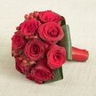 Stanmore's local flair shines through in this exquisite bouquet, where rich, velvety red roses and polished hypericum berries come together in a tightly sculpted embrace. About ten striking roses, each in full, flawless bloom, are arranged with meticulous attention and surrounded by sweeping, lush green leaves that add both shelter and drama. The arrangement is completed with pops of festive, glistening red berries, peeking through the roses for tactile intrigue and a sense of celebration. The stems are skillfully tied and finished with an opulent red satin ribbon-its luster catching the light and providing a secure, elegant handle. The bouquet rests on a creamy linen background, reminiscent of the bright, inviting spaces in Stanmore's beloved event venues. Gentle, diffused light highlights the deep reds and fresh greens, casting soft shadows and lending an air of understated grace. This creation, perfect for Stanmore weddings, anniversaries, or surprise moments of love, is a harmonious blend of timeless beauty and contemporary polish-crafted to evoke lasting memory and emotion in the heart of the community.