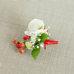 Resting flat on a warm, oatmeal-coloured fabric that resembles linen, this boutonniere is an exercise in quiet contrasts and thoughtful restraint. The centrepiece is a pristine white phalaenopsis orchid, its broad petals arranged like satin folds and opening to expose a soft yellow-orange throat that reads as gentle and composed. Encircling the orchid, fine sprays of gypsophila form a delicate, cloud-like halo; their tiny white flowers add an ephemeral, romantic texture that softens the design. Bright red hypericum berries cluster low in the composition, their round, glossy forms supplying a joyful, seasonal punctuation to the otherwise pale palette. A few pale green buds are visible among the stems, promising further life and a subtle green note, while deep green salal leaves are placed to cradle and ground the blooms, their sheen and shape lending a polished botanical backbone.
The stems are bound with a rich red satin ribbon, tied into a small, precise knot with a short tail angled to the right, giving the piece an understated flourish. Gentle, side-lit illumination reveals the linen grain beneath and the soft contours of each petal and berry, creating a tactile sense of texture and depth. Imagined on a lapel at a local Stanmore wedding near Bentley Priory or for a formal evening at a nearby village hall, this boutonniere offers calm elegance and a handcrafted sensibility that speaks of floral expertise and thoughtful local sourcing.