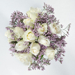 The bouquet in this photograph is captured from directly above, revealing a harmonious, circular composition that combines white roses with soft lavender Limonium. At its centre, roughly a dozen roses form a close, domed cluster, each head turned slightly in a different direction so that you can see a range of blooming stages. Some roses remain relatively closed, their outer petals gently folded in; others are half-open, with smooth spirals of creamy white unfolding; a few are fully open, showcasing intricate, layered hearts with just a whisper of ivory and pale yellow in their depths. Around and between these roses, fine sprays of Limonium radiate outwards, their tiny lavender-purple flowers forming airy, cloud-like plumes that soften the edges of the arrangement. The texture interplay is subtle yet distinct: the roses look sumptuous and velvety, while the statice appears light and slightly papery, almost like pressed wildflowers. Small hints of green stems and minimal foliage peek out from the base, offering stability and a touch of natural contrast without detracting from the refined colour palette. Set against a plain, bright white background, the bouquet feels especially serene and contemplative, as though floating in soft light. This is the kind of arrangement often chosen in Stanmore when families wish to express condolences with quiet elegance, whether it is being sent to a house near Marsh Lane, a service by Stanmore station, or a memorial gathering overlooking the greenery of Canons Park. The combination of white roses and lavender Limonium speaks gently of remembrance, peace, and the hope of comfort during a difficult time.