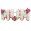 A solemn, tender tribute formed as three large block letters spelling MUM, photographed against a clean white backdrop so every detail reads clearly. Each letter is densely built from small, pristine white chrysanthemums whose feathery petals overlap to create a soft, cloud-like surface that suggests quiet purity and remembrance. The outer edges of every letter are gently framed with a ruffled pale pink ribbon or fabric trim, the soft blush adding a motherly warmth and a subtle halo of colour against the white blooms. Between the letters a dark green supporting frame peeks through, the structural rods giving the standing tribute a measured, upright dignity. To bring life and contrast to the composition, three compact posies of vivid fuchsia-pink roses are tucked into the arrangement: one nestled at the upper left shoulder of the first M, another placed at the lowest curve of the U, and a final cluster resting at the upper right of the second M. Each rose cluster is finished with glossy fern-like greenery and small coral to reddish hypericum berries, their shiny skins and warm tones catching light and adding tactile sparkle. The overall texture ranges from the crisp, papery mums to the velvety roses and smooth berries, creating a comforting rhythm under soft, even studio lighting. This is the kind of personal, dignified memorial piece families in Stanmore often choose for a funeral service, wake, or graveside farewell - a design that reads as both respectful and deeply affectionate, holding space for scent, memory, and gentle consolation.